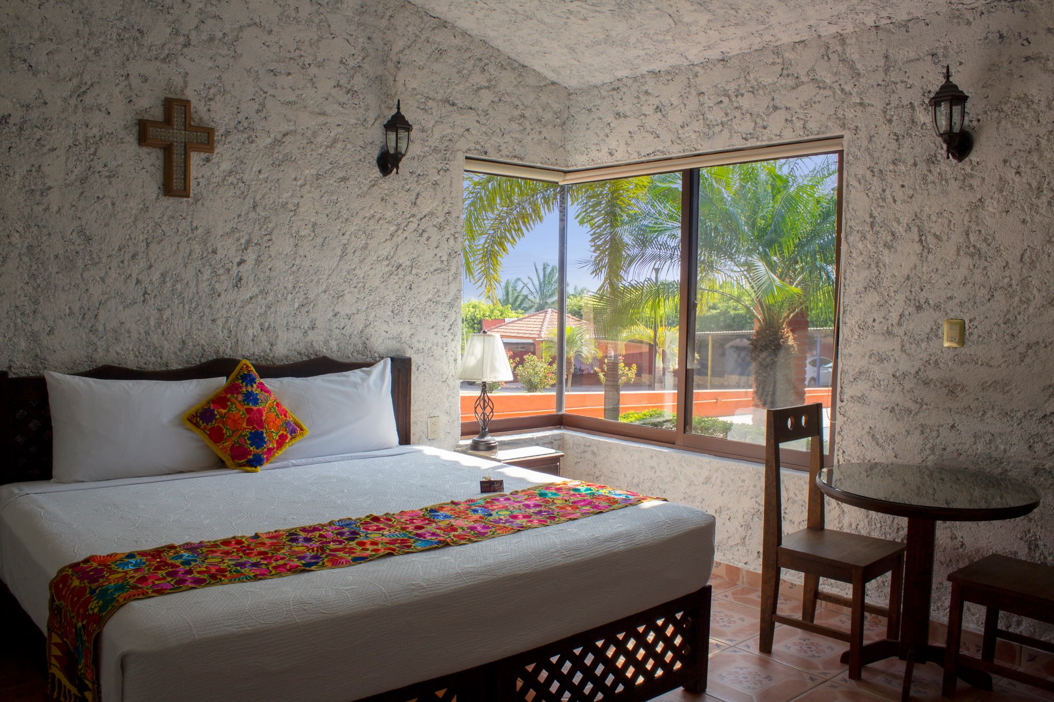 Rustic Mexican-style hotel room with embroidered accents, terracotta tiles, tropical garden view, and workspace—ideal for MICE accommodations, incentive travel, and cultural retreats in heritage destinations.