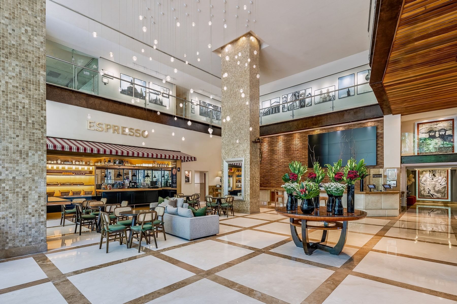 The modern, luxurious lobby of the Grand Fiesta Americana Guadalajara, featuring a sleek 'Espresso' café area with comfortable seating and high ceilings with cascading light fixtures. This spacious area is ideal for informal networking, small group meetings, or conference registration. The design emphasizes high-end aesthetics, making it perfect for executive retreats and premium incentive groups.