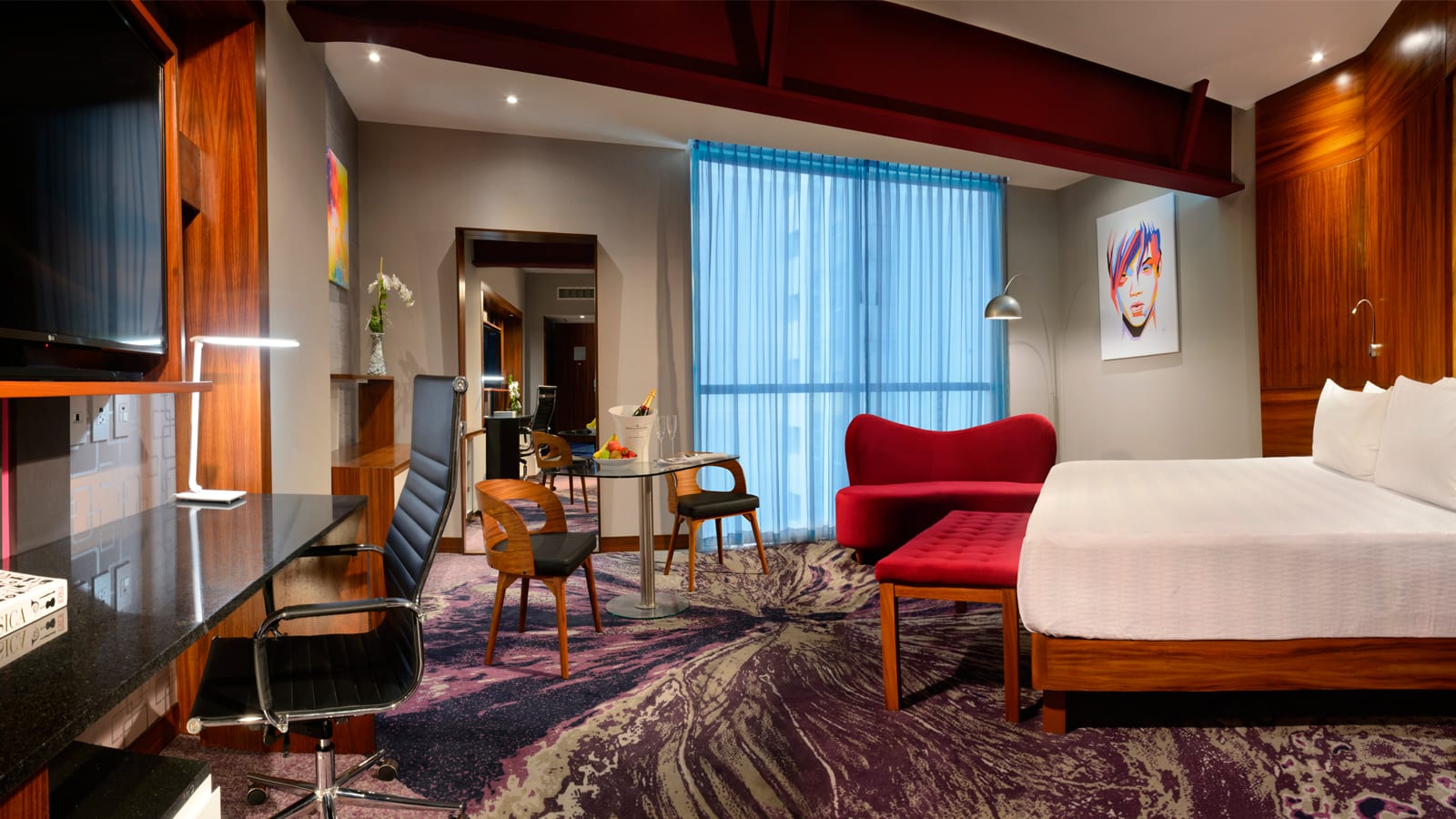 A stylish and modern guest room or suite at the Hard Rock Hotel Guadalajara, featuring contemporary art, rich wood paneling, a king-sized bed, and a dedicated workspace (ideal for business travelers and executives). The vibrant color scheme and unique furnishings emphasize a high-end experience, making this a perfect room for VIP speakers, incentive winners, or key MICE delegates seeking luxury accommodations.