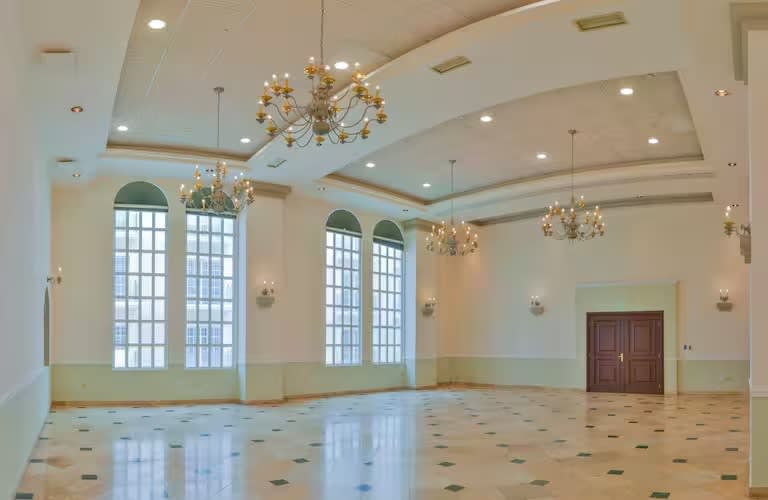 Elegant MICE function room at Villa Mercedes Mérida: View of a spacious, empty ballroom featuring large arched windows, marble flooring, sophisticated chandeliers, and high ceilings. The room is ideal for customizable setup for conferences, corporate events, and gala banquets up to 350 guests.