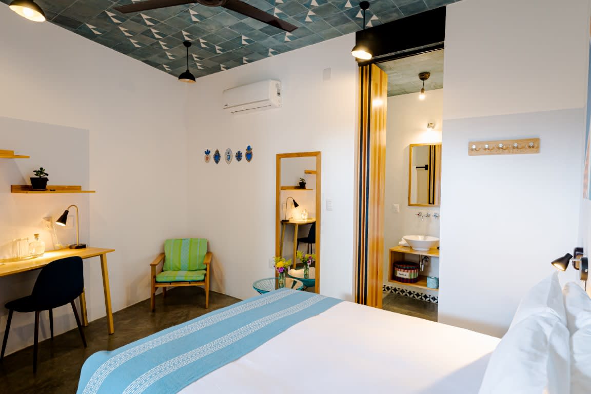 Stylish bedroom at Hotel con Corazón Oaxaca with rustic textures, mountain-view balcony, and cozy seating—ideal for MICE guests attending events or incentive programs.