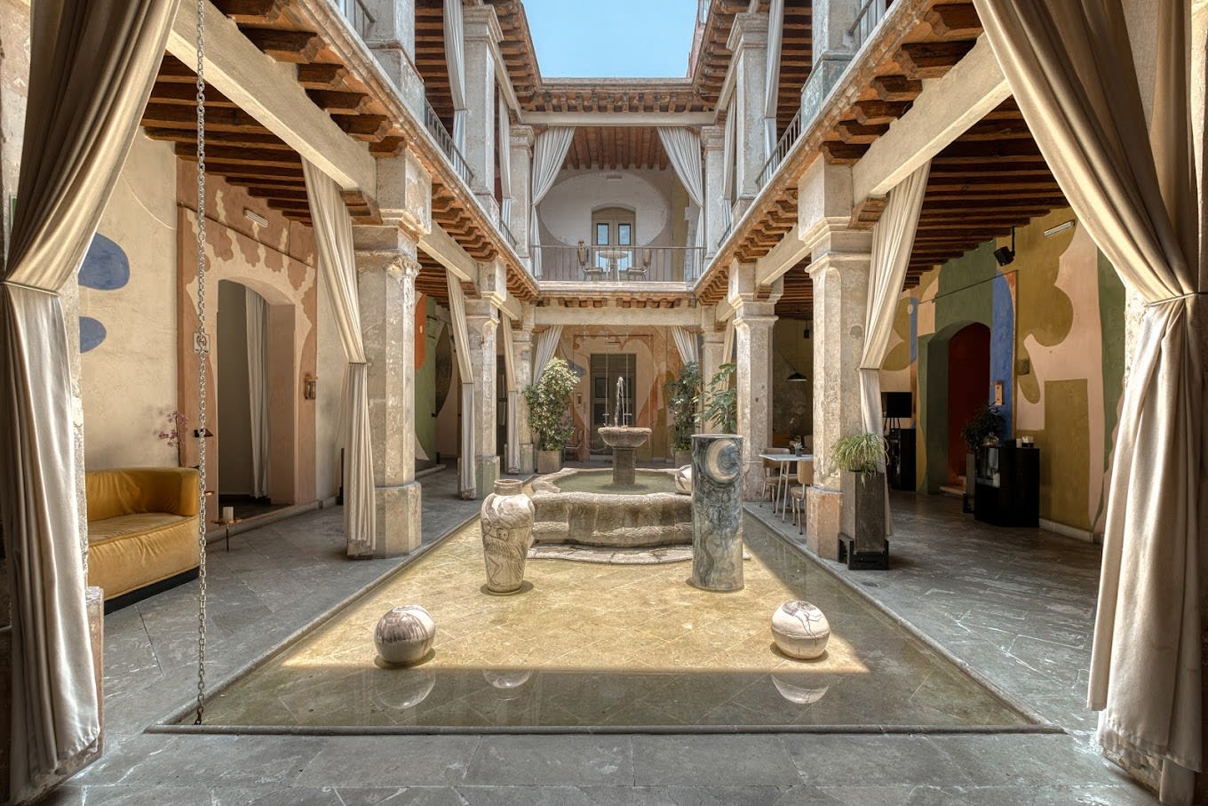Elegant courtyard at Hotel Pug Seal Oaxaca with sculptural fountain, murals, and modern furnishings—ideal for MICE retreats, boutique gatherings, and cultural incentive programs.