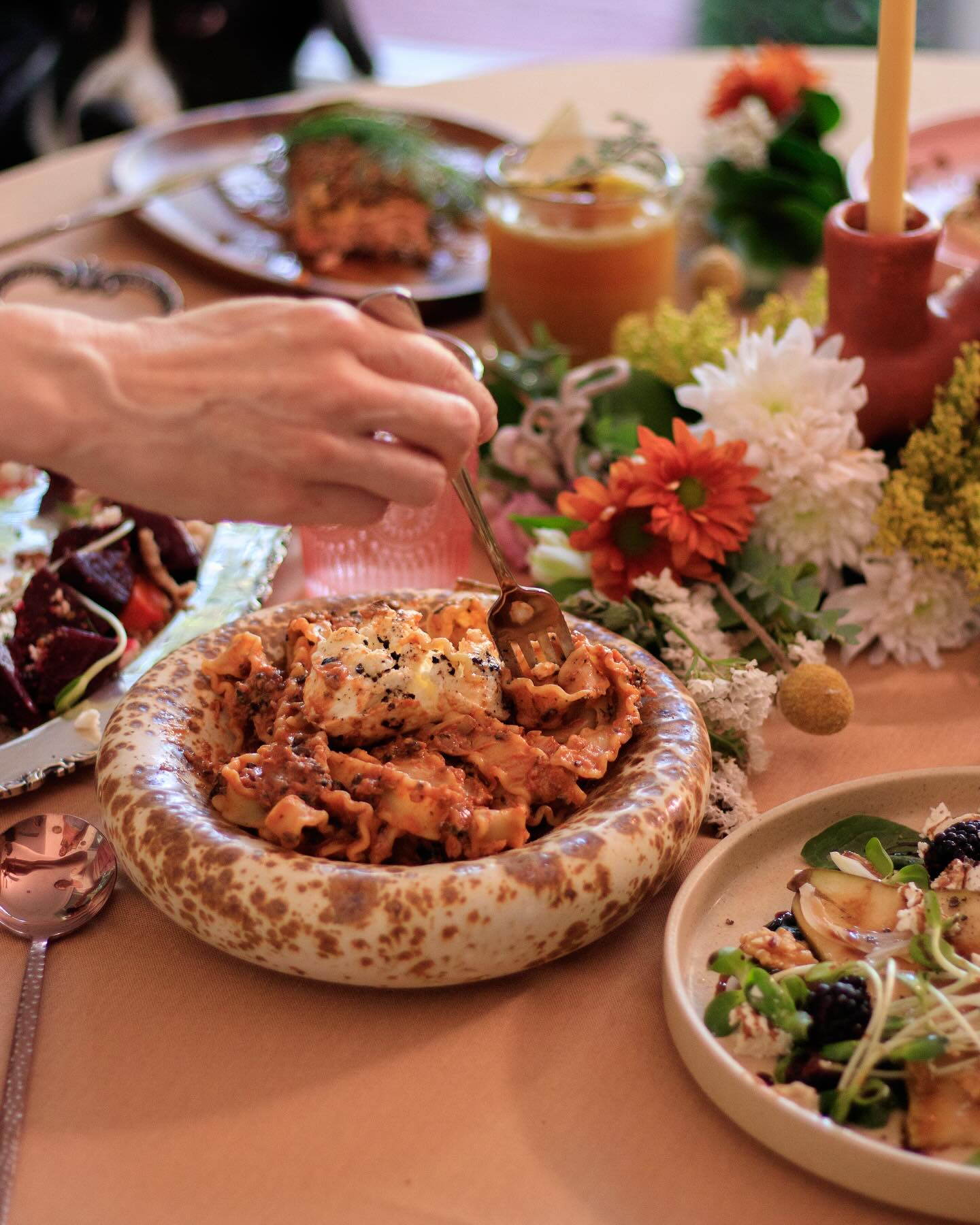 A close-up shot of a chef's hands in a denim apron, carefully peeling garlic over two pans containing sliced red and orange vegetables. This showcases the detail and fresh ingredients involved in corporate catering and private culinary services for MICE events.