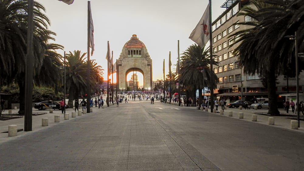 A wide view of the Monument to the Revolution in Mexico City at sunset. People are walking on the pedestrian pathway leading to the monument, which is a key landmark and a great location for MICE industry events and incentive travel.
