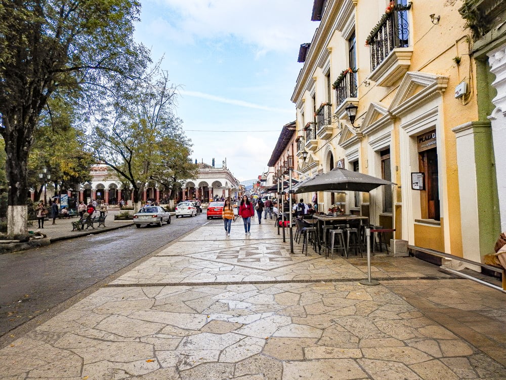 A wide pedestrian street in San Cristobal de las Casas, Chiapas, with historic buildings, a plaza, and a cafe. Ideal for MICE industry travel and events.