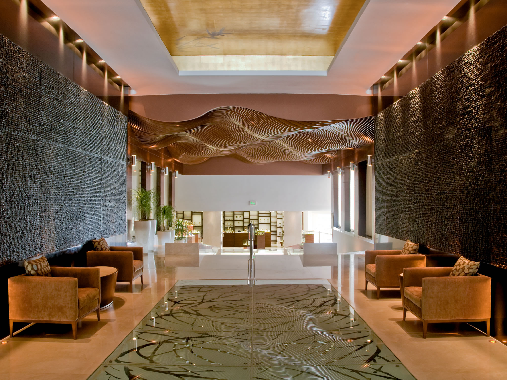 A spacious, elegantly designed spa reception and lounge area at Gem Spa, featuring textured walls, modern brown armchairs, and abstract overhead lighting design. The luxurious setting is ideal for promoting high-end MICE venue amenities and exclusive environments for corporate event networking or pre-treatment relaxation during an incentive trip.