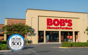 Bob's Discount Furniture store exterior with large red signage, clear glass entrance, and a 2026 Home Furnishings 500 award badge overlay.