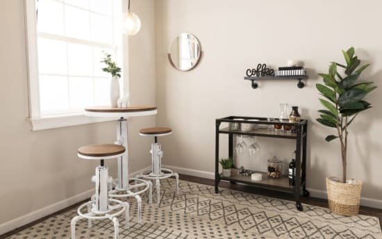 Minimalist coffee nook with white and wood adjustable bar stools, a round table, black metal bar cart with glassware, and a potted plant.