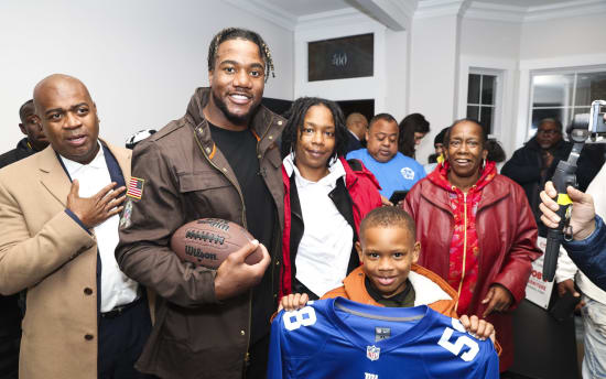 Group of people indoors, one holding a Wilson football, another child holding a blue New York Giants NFL jersey with number 58, casual and winter clothing.