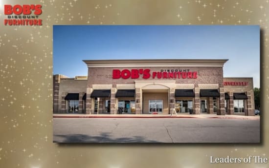 Bob's Discount Furniture storefront with beige brick facade, large red and black signage reading "BOB'S DISCOUNT FURNITURE," black window awnings, and clear blue sky background. Text in image includes "BOB'S DISCOUNT FURNITURE" in top left corner and "TOP 100 U.S. FURNITURE STORES" in top right corner, with "Leaders of The Pack" at bottom right.