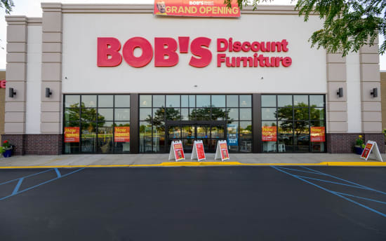 BOB'S Discount Furniture storefront with large red signage, glass entrance, and multiple "Now open!" and "Grand Opening" promotional signs.