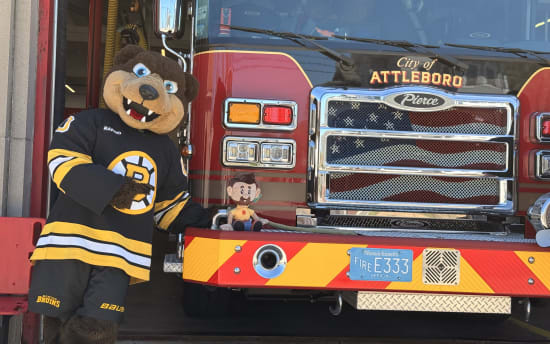 A person in a Boston Bruins mascot costume stands next to a red City of Attleboro fire truck with a Massachusetts license plate reading "FIRE E333."
