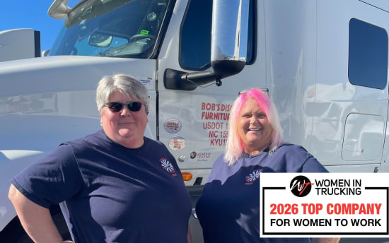 Two women truck drivers standing in front of a white semi-truck wearing navy blue Women in Trucking t-shirts. Text overlay reads: "Women in Trucking 2026 Top Company for Women to Work."