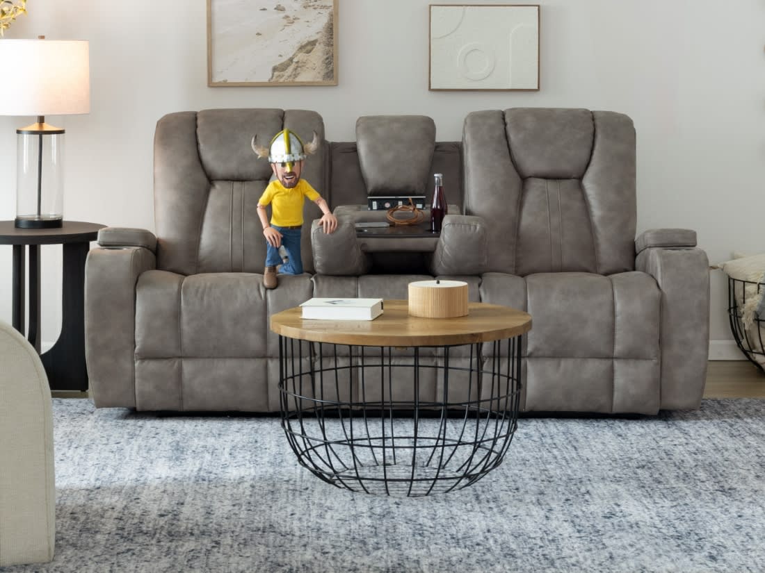 Gray reclining three-seat sofa with center console, wooden round coffee table with metal wire base, modern living room setup with side lamp and wall art.