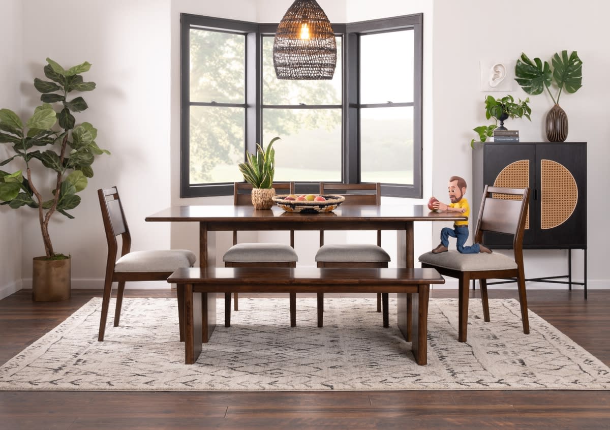 Modern dining room set with dark wood table, cushioned chairs, and bench on patterned rug, featuring large bay window and decorative plants.
