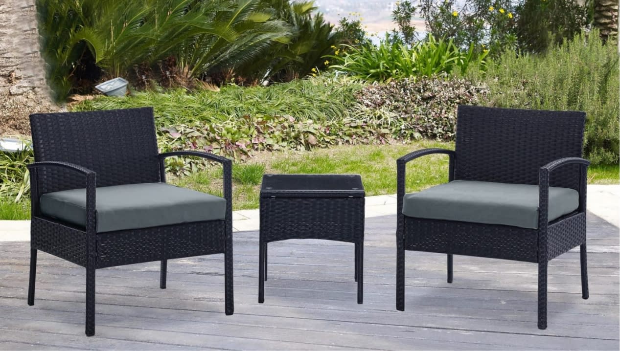 Outdoor patio set with two black wicker armchairs featuring gray cushions and a matching square wicker side table on a wooden deck.