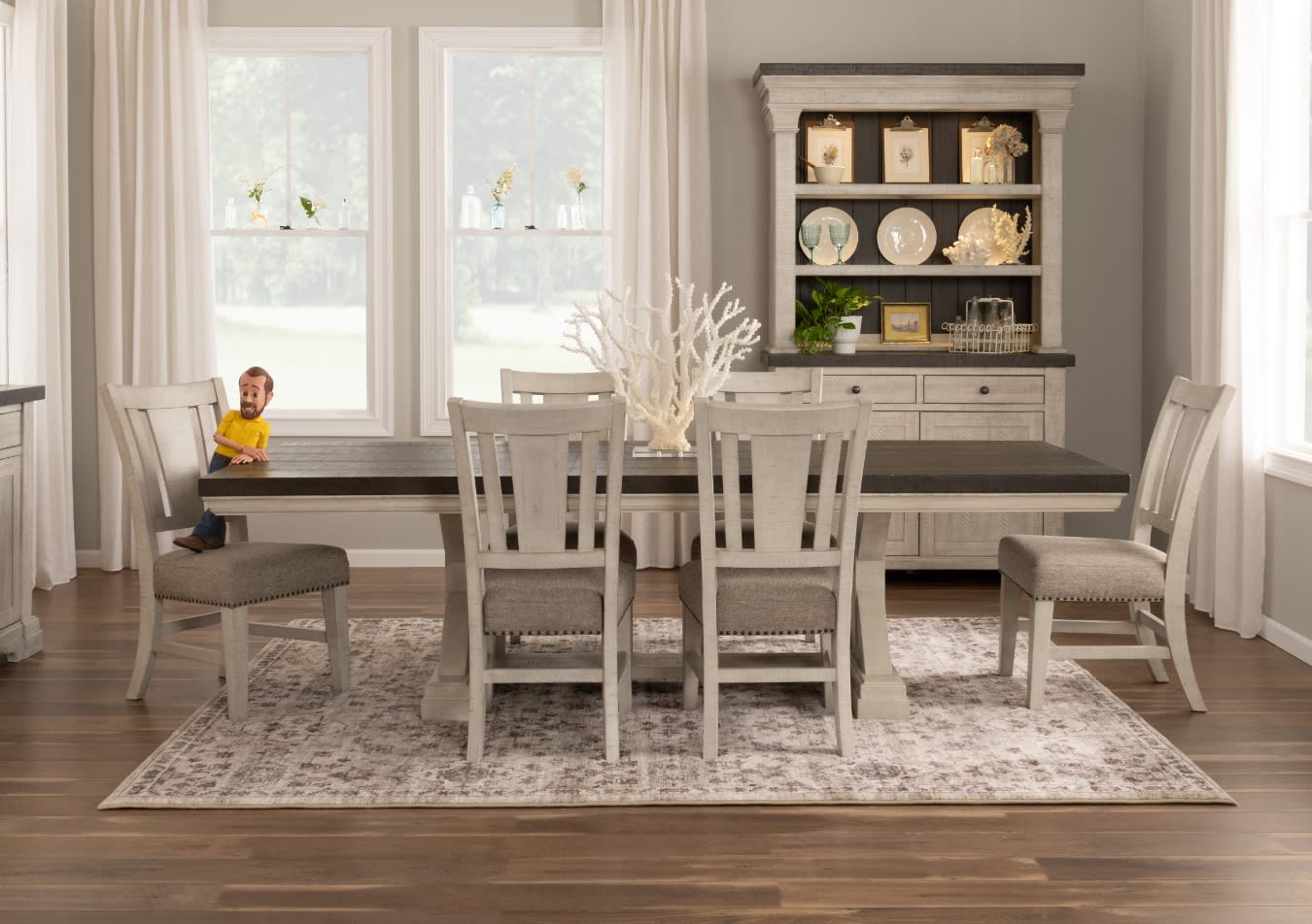 Dining room set with gray wooden table and six matching upholstered chairs on patterned rug, featuring decorative coral centerpiece and hutch with plates and plants.