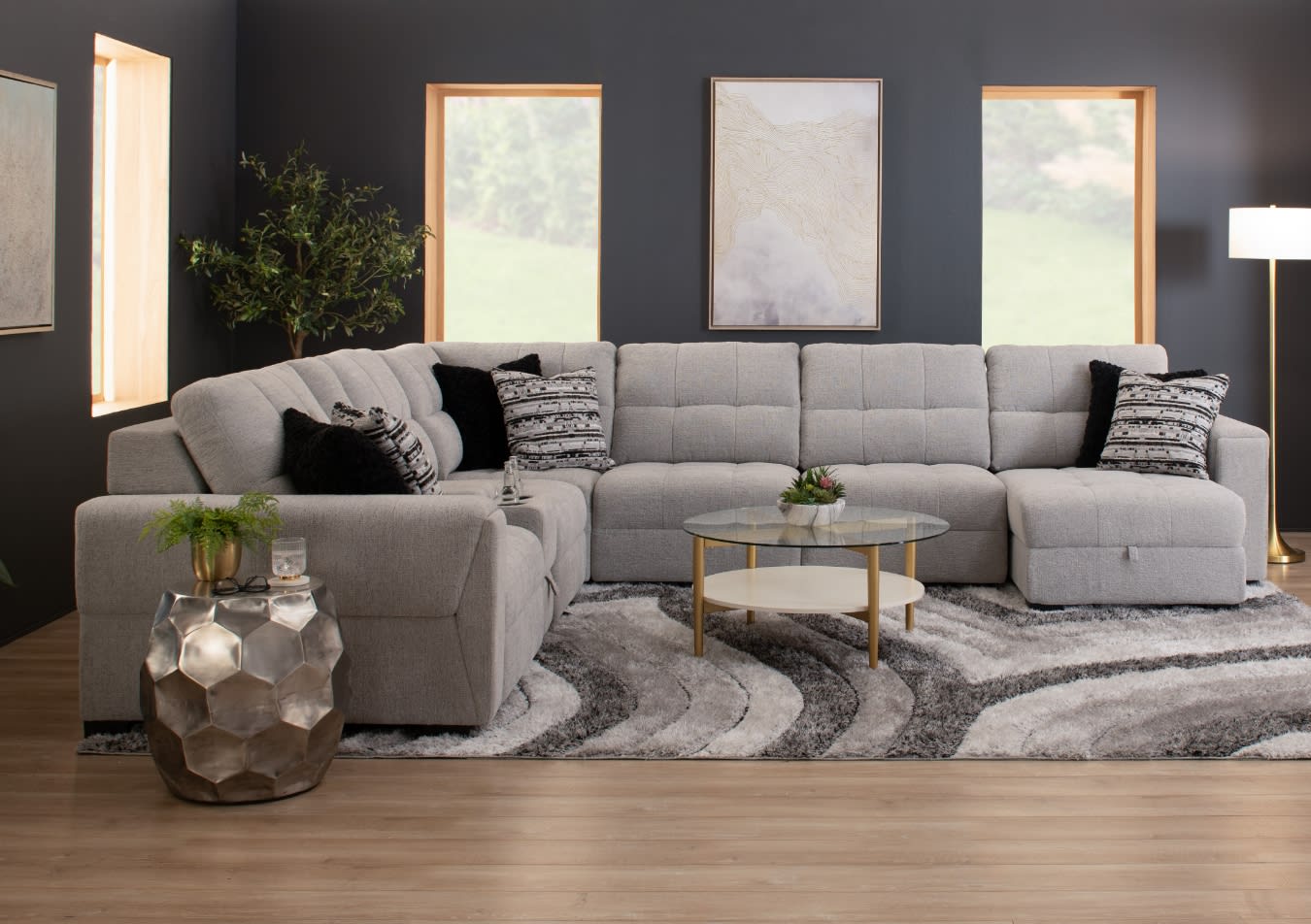 Modern gray fabric sectional sofa with tufted cushions, black and patterned throw pillows, glass and gold coffee table, and metallic side table in a stylish living room.