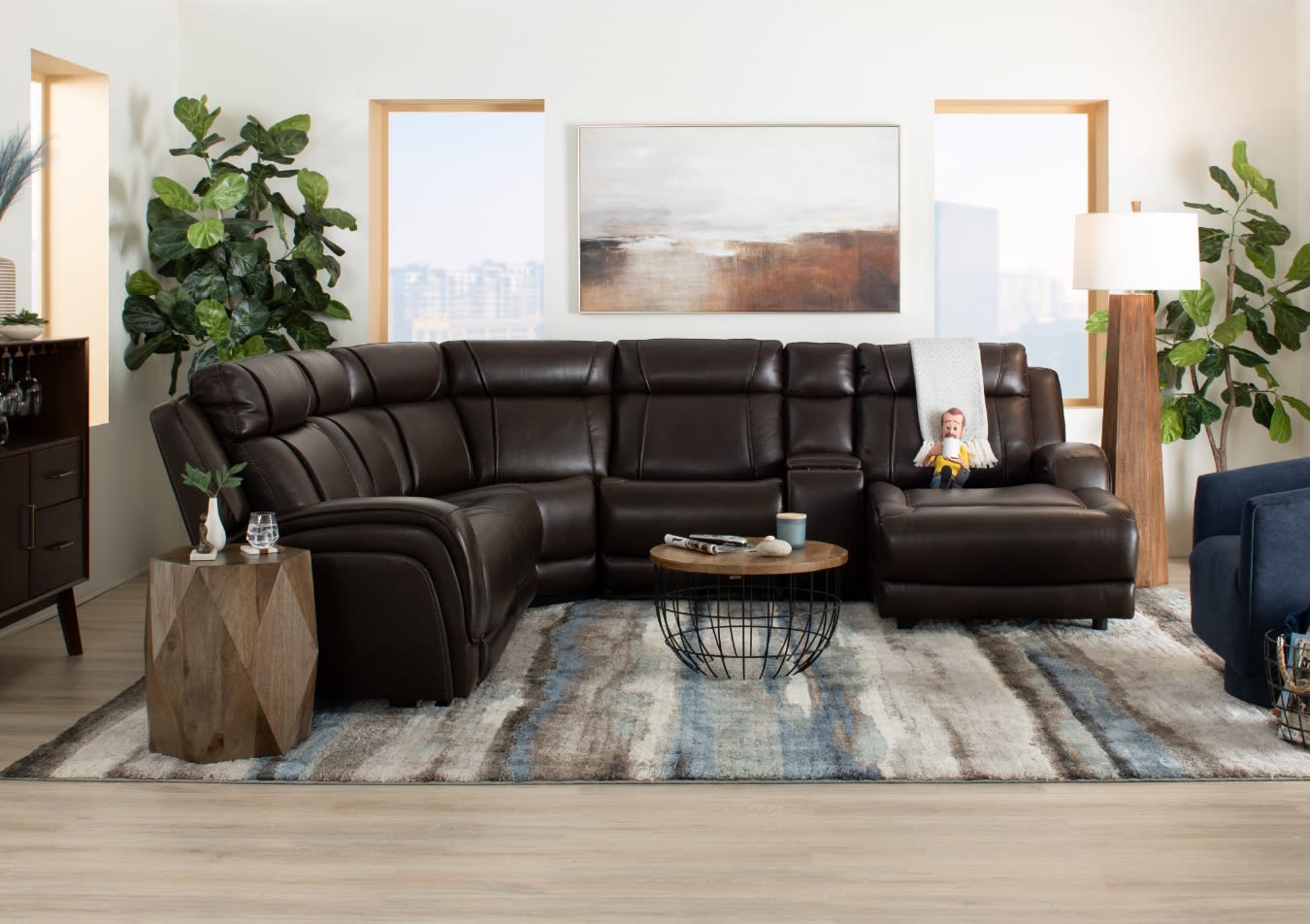 Dark brown leather sectional sofa with plush cushioning and a chaise lounge, set on a patterned area rug in a modern living room with wooden accents and greenery.