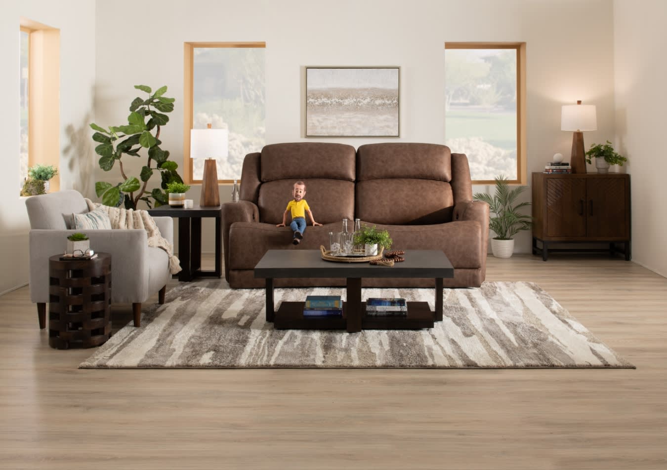 Modern living room with a brown leather reclining sofa, gray fabric armchair, dark wood coffee table, and neutral patterned area rug on light wood flooring.