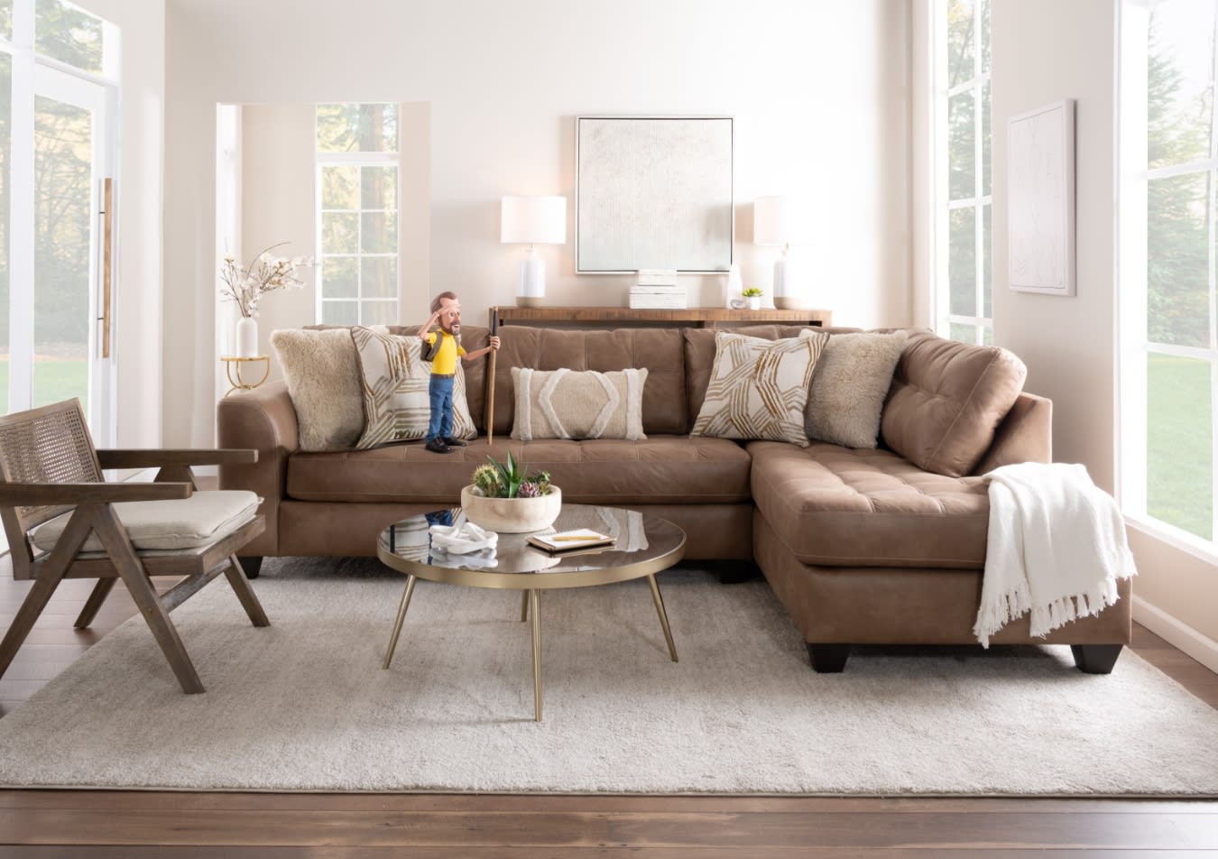 Brown leather sectional sofa with beige and patterned throw pillows, a round glass coffee table with plants, and a wooden armchair in a bright living room.