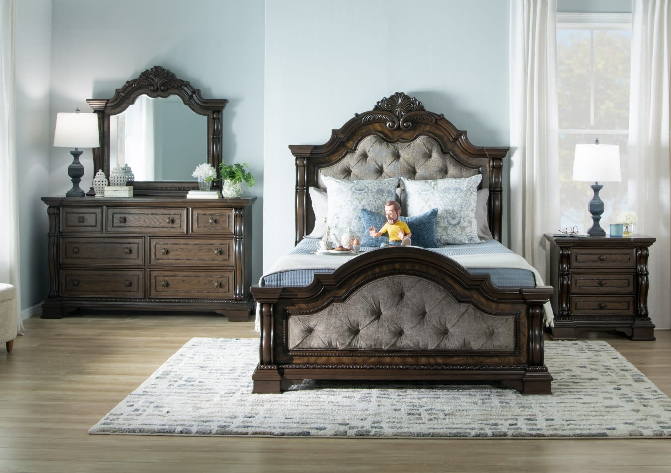 Traditional dark wood bedroom set with tufted upholstered headboard and footboard, matching dresser with mirror, nightstand, and table lamps on a light patterned rug.