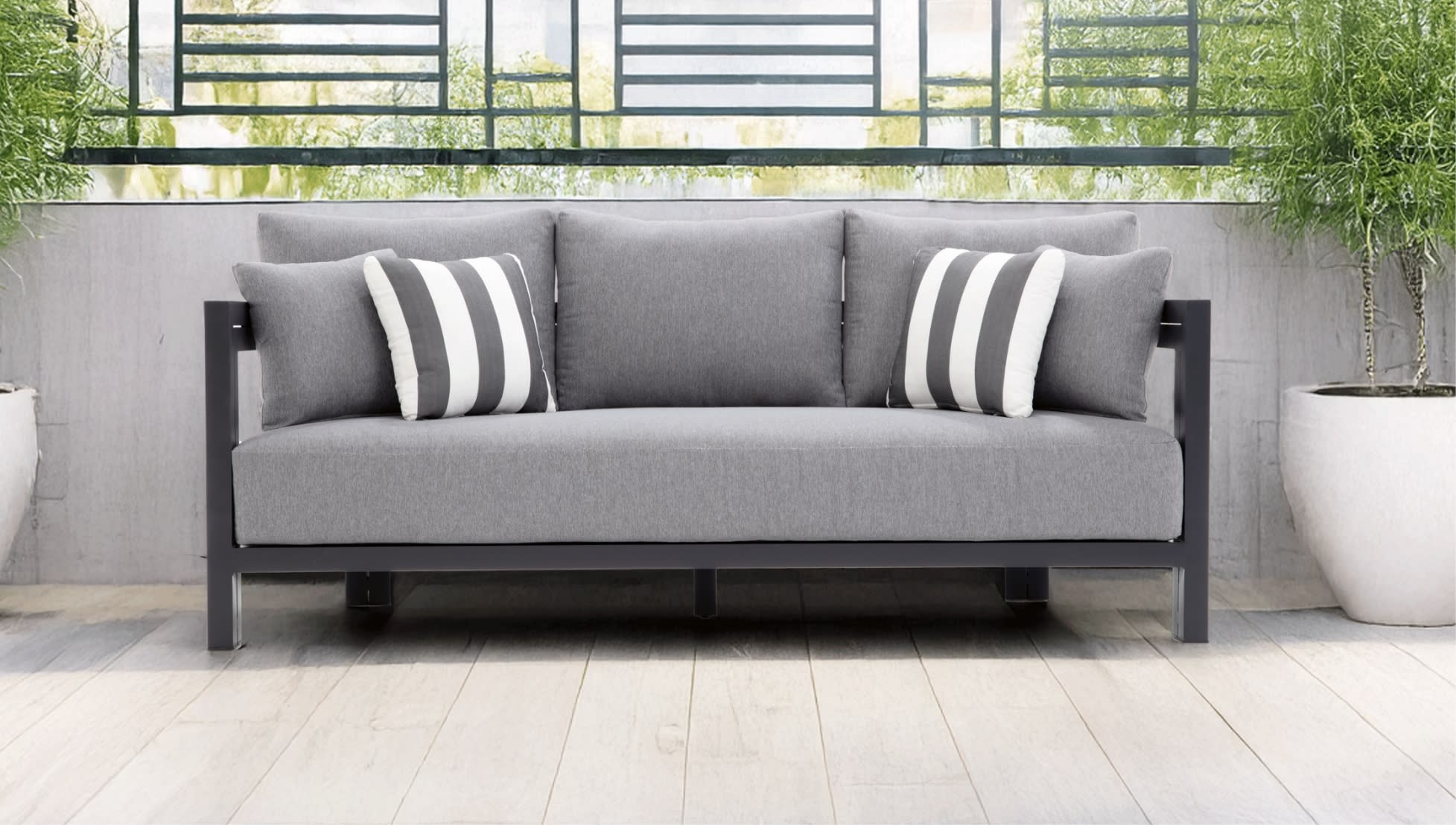 Modern outdoor gray fabric sofa with black metal frame, featuring four cushions and two striped accent pillows, set on light wood flooring.