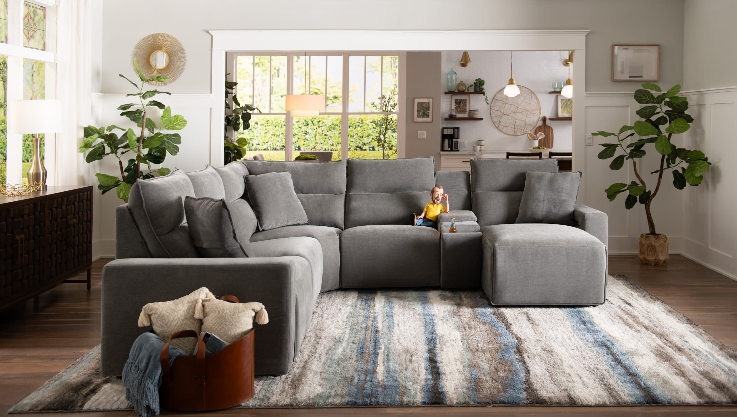 Gray sectional sofa with plush cushions and chaise lounge on a textured area rug in a modern living room with plants and natural light.