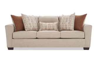Beige fabric sofa with three seat cushions and five decorative pillows in rust and patterned beige tones, featuring dark wooden legs and a modern design.