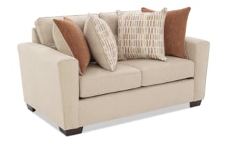 Beige fabric loveseat sofa with dark wooden legs, featuring four decorative throw pillows in rust and patterned beige tones, modern style.