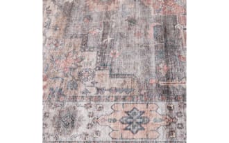 Vintage-style area rug with a distressed pattern featuring muted gray, blush pink, and cream tones, floral and geometric motifs, and a soft textured look.