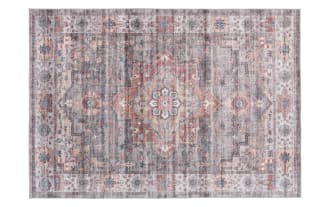 Vintage-style area rug with a distressed pattern featuring muted gray, blush pink, and cream tones, floral and geometric motifs, and a soft textured look.