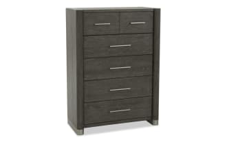 Dark gray wooden chest of drawers with five drawers, sleek metal handles, rounded vertical edges, and metal feet, modern bedroom storage.