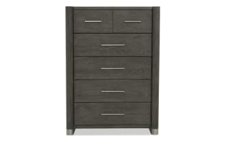Dark gray wooden chest of drawers with five drawers, sleek metal handles, rounded vertical edges, and metal feet, modern bedroom storage.