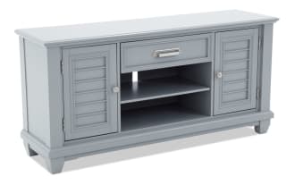Gray wooden TV stand with two shutter-style cabinet doors, one center drawer, and open shelving with cable management hole.