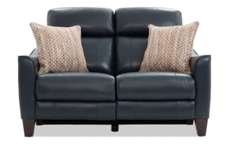 Dark blue leather loveseat with two patterned beige throw pillows, featuring padded armrests and wooden legs, ideal for modern living rooms.