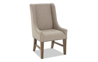 Upholstered beige fabric dining chair with high back, wooden legs, and nailhead trim, designed for comfort and style.