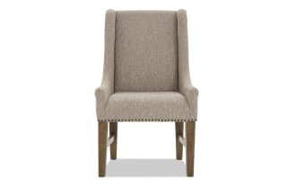 Upholstered beige fabric dining chair with high back, wooden legs, and nailhead trim, designed for comfort and style.