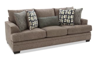 Brown fabric sofa with three large seat cushions and five decorative pillows, featuring a mix of geometric and textured patterns, modern style.