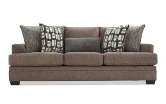 Brown fabric sofa with three large seat cushions and five decorative pillows, featuring a mix of geometric and textured patterns, modern style.