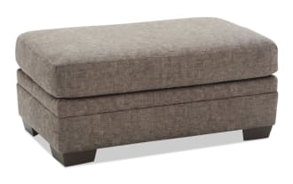 Rectangular brown fabric ottoman with plush cushioned top and dark wooden block legs, suitable for living room seating or footrest.