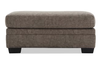 Rectangular brown fabric ottoman with plush cushioned top and dark wooden block legs, suitable for living room seating or footrest.
