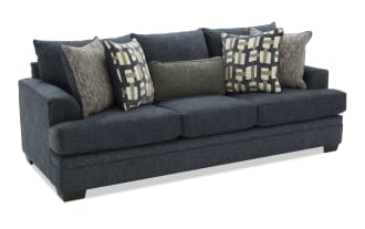 Dark blue fabric sofa with three seat cushions and six decorative pillows in geometric and textured patterns, modern living room furniture.