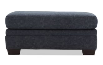 Dark blue fabric upholstered rectangular ottoman with cushioned top and wooden block legs, suitable for living room seating or footrest.