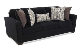 Dark gray fabric sofa with three seat cushions and five decorative pillows in brown and patterned beige, ideal for modern living rooms.