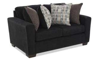 Black fabric loveseat sofa with wide arms, wooden block legs, and four decorative pillows in brown and patterned beige tones, modern style.
