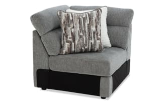 Modern corner armchair upholstered in grey fabric with black base accents, featuring two decorative cushions in white and brown abstract patterns for living room seating.