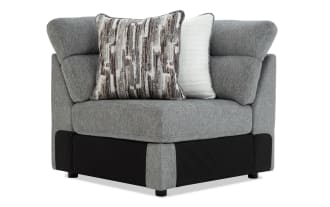 Modern corner armchair upholstered in grey fabric with black base accents, featuring two decorative cushions in white and brown abstract patterns for living room seating.