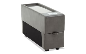 Gray leather storage ottoman with visible stitching, rectangular shape, and two black cylindrical legs, shown from the side.