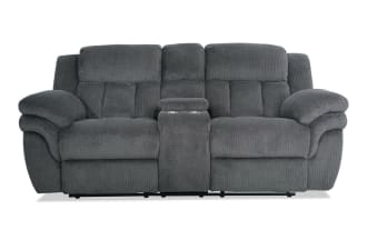 Dark gray plush fabric reclining loveseat with padded armrests, high back cushions, and a center console with cup holders, designed for comfort and relaxation.